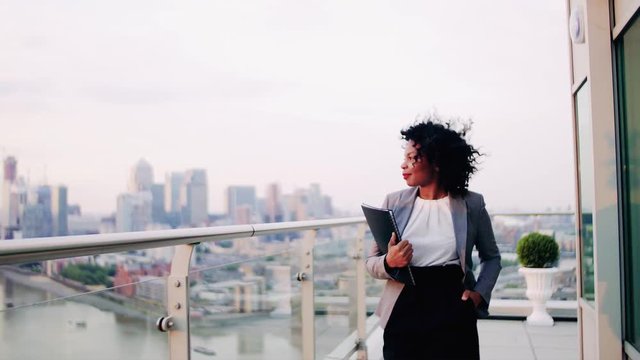 A portrait of a businesswoman walking on a terrace at sunset, holding notes.