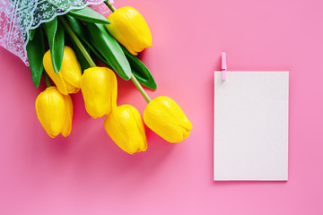 Artificial yellow tulips with white paper card on pink background for nature decoration and springtime concept