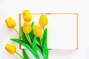 Artificial yellow tulips with blank notebook on white background for workspace, nature decoration and springtime concept