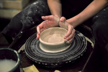 Hands in clay shape the product on a potter's wheel, close-up