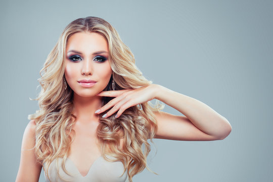 Young blonde woman fashion model with long curly hair, makeup and manicure on blue background