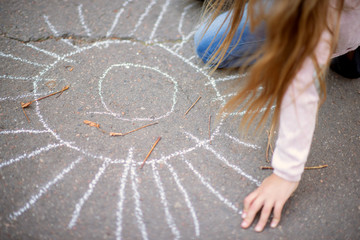 Obraz premium Little girl is draws sun chalk on the floor in the park
