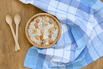 Bowl of muesli, two spoons and towel on wooden table.