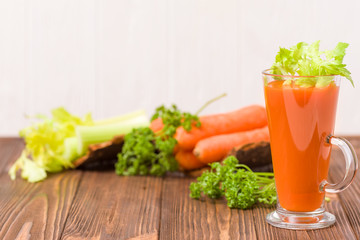 Carrot and celery juice with fresh vegetables on bark plates on wooden background.