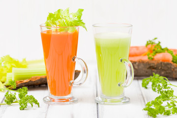 Carrot and celery juice with fresh vegetables on bark plates on wooden background.