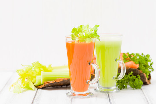 Carrot and celery juice with fresh vegetables on bark plates on wooden background.