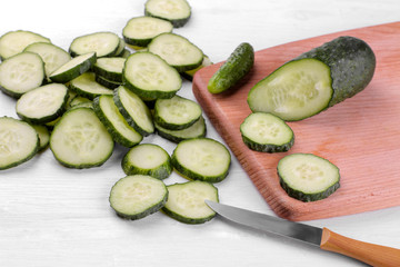 A lot of sliced cucumber slices on a cutting board with a knife on a white wooden table