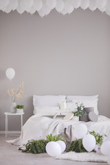 White balloons under the ceiling of stylish grey bedroom with comfortable bed with white bedding and grey accents, real photo with copy space on the empty wall