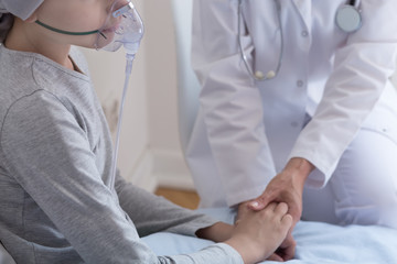 Closeup of sick kid with oxygen mask and doctor holding her hand in hospital © Photographee.eu