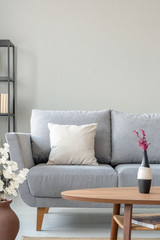 Heather in vase on the wooden table next to comfortable grey couch in monochromatic living room,...