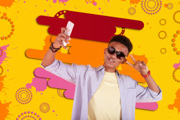 Cool teenager. Cool teenager wearing dark sunglasses depicting near colorful background making selfie using his smartphone