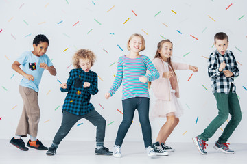 Smiling girls and boys dancing together in the school against colorful wallpaper