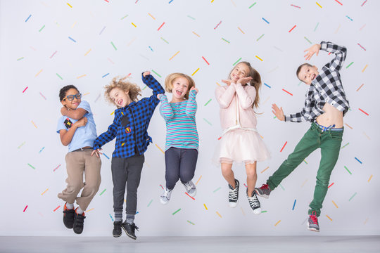 Happy multicultural group of kids jumping against colorful wallpaper