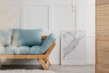 Blue sofa with pillows next to map in white frame in elegant living room interior of minimal house, real photo with copy space on the empty wall - obrazy, fototapety, plakaty