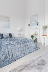 Posters and plants in white simple bedroom interior with blue bed and lamp on cabinet. Real photo