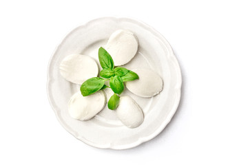 An overhead photo of a white plate with fresh basil leaves and Mozzarella cheese, shot from the top on a white background with copy space