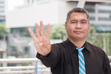 happy old man pointing up four fingers; retired pensioner counting, numbering with finger point; senior old man points four fingers up portrait; southeast old senior man model