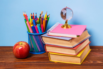 On a wooden table books, an apple and a globe