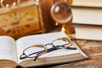 An open book with glasses along with an ancient clock and globe