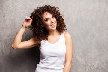 Fototapeta na wymiar Portrait of beautiful cheerful girl with flying curly hair smiling laughing looking at camera over gray background.