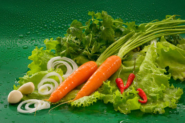 Vegetables - carrots, red hot chili peppers, garlic, lettuce, parsley, onion rings on a green background