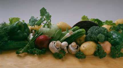 Vegetables - cucumber, onion, potatoes, broccoli, kohlrabi, mushrooms, bean pods, pepper, garlic, lettuce, parsley, dill on a light background and on a wooden table