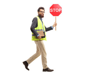 Man in a safety vest holding a stop traffic sign walking and looking at the camera