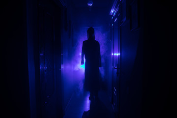 Fototapeta premium Creepy silhouette in the dark abandoned building. Horror Halloween concept. Dark corridor with silhouette of horror person standing in center. Toned light and fog on background. Selective focus