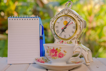 Cup of coffee, open notebook with blank pages, vintage clock, pen,  on green background  Still life, concept of business