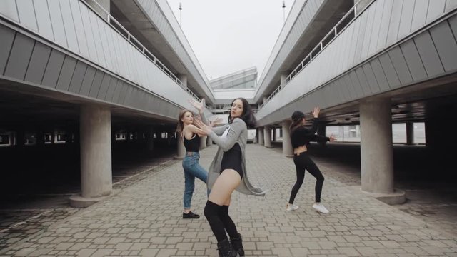 Attractive female dancers dancing and performs modern vogue or hip hop dance in parking lot, posing, contemporary freestyle in different styles of clothing, industrial urban environment