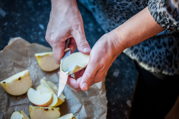 A woman cooking apple pie  and cutting apple. Preparing healthy food. Hands holding knife and slicing apple in kitchen. Process of preparation of apple pie. Close up, soft focus.