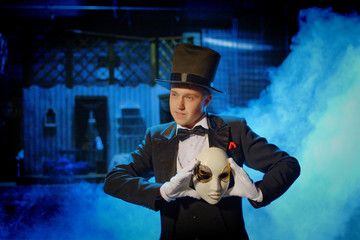 a young actor in a tuxedo holding a theatrical mask in a hat