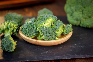 Beautiful broccoli florets on a wooden plate on a slate board.