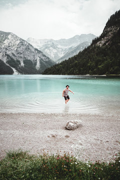 junger mann mit Hut und Tank-Top steht im Wasser des Plansees