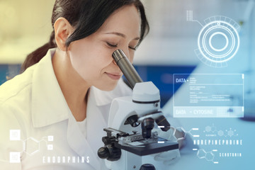 Looking through microscope. Calm attentive biologist thoughtfully smiling while looking at the...