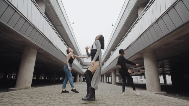 Girls in different styles of clothing dancing and performs modern hip hop or vogue dance in parking lot, posing, contemporary freestyle, industrial urban environment