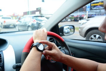 a man  holding the steering wheel with the left hand and touch  the watch with the right hand during the rush traffic time of the morning  and white Glare light outside the car