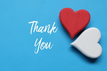 Wooden red and white heart on blue background written with THANK YOU.