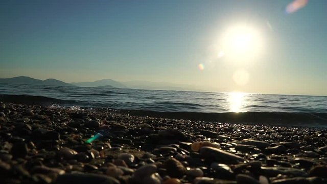 Sommer, Sonne und Meer: Sanfte Wellen pl&auml;tschern an den Kieselstrand im Gegenlicht der untergehenden Sonne
