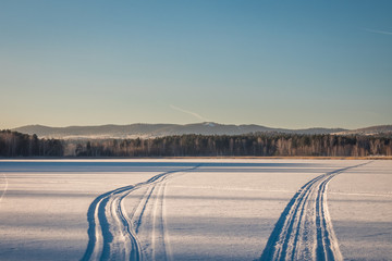traces of a snowmobile in the fresh snow on a frozen lake