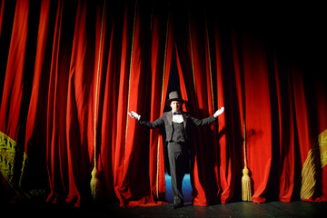 Actor in a tuxedo and hat looks behind the theater curtain