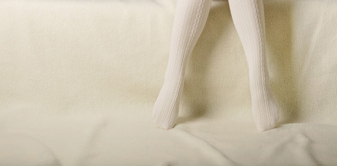 Female legs in warm white knitted tights on a white background made of faux fur.