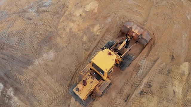Yellow excavator or bulldozer works on construction site with sand, aerial or top view.