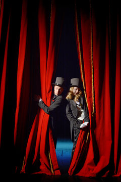 Actor and actress in tuxedos open theater curtain