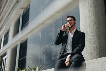 Smiling business person taking on mobile phone sitting outdoors