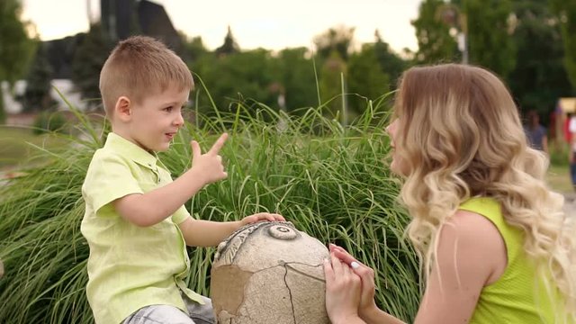 Mother and little son play in the Park in warm summer weather with a stone statue of a turtle.