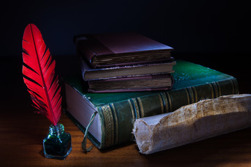 Red quill pen and a rolled papyrus sheet on a wooden table with old books