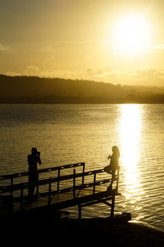man taking photo of a woman on a pier at sunset