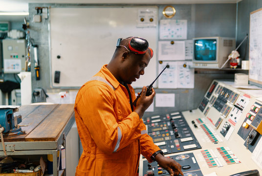 African marine engineer officer in engine control room ECR. He speaks with VHF or UHF portable radio. Ship communication routine