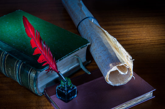 Red quill pen and a rolled papyrus sheet on a wooden table with old books